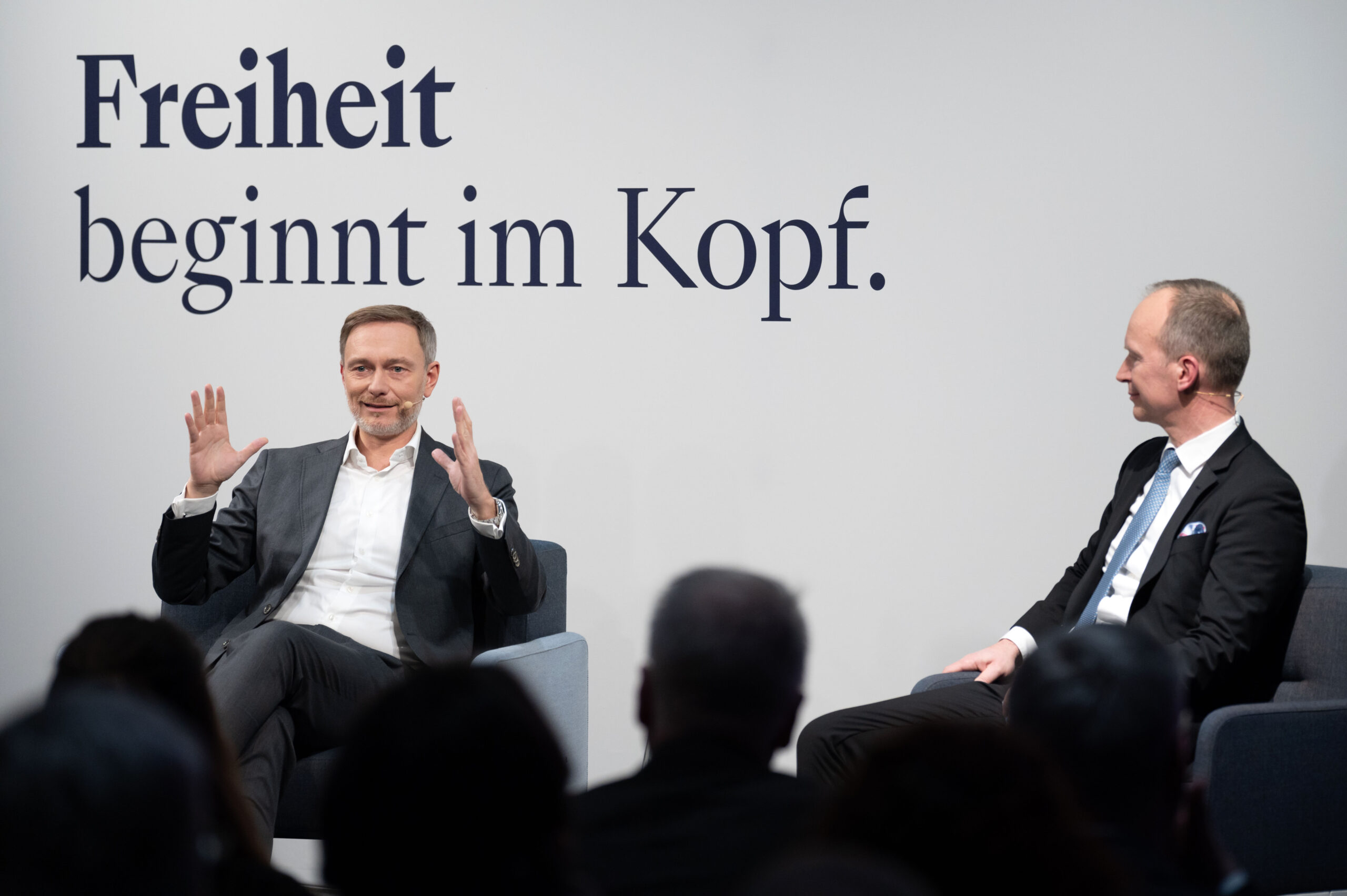 Zwei Männer im Anzug diskutieren vor Publikum, Hintergrund mit Schriftzug „Freiheit beginnt im Kopf.“