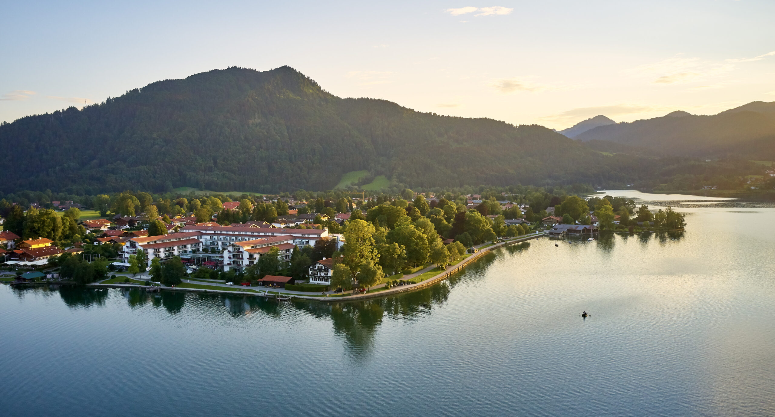 Althoff Seehotel Überfahrt am Tegernsee mit Alpenpanorama, Uferpromenade und reflektierendem Wasser bei Sonnenuntergang