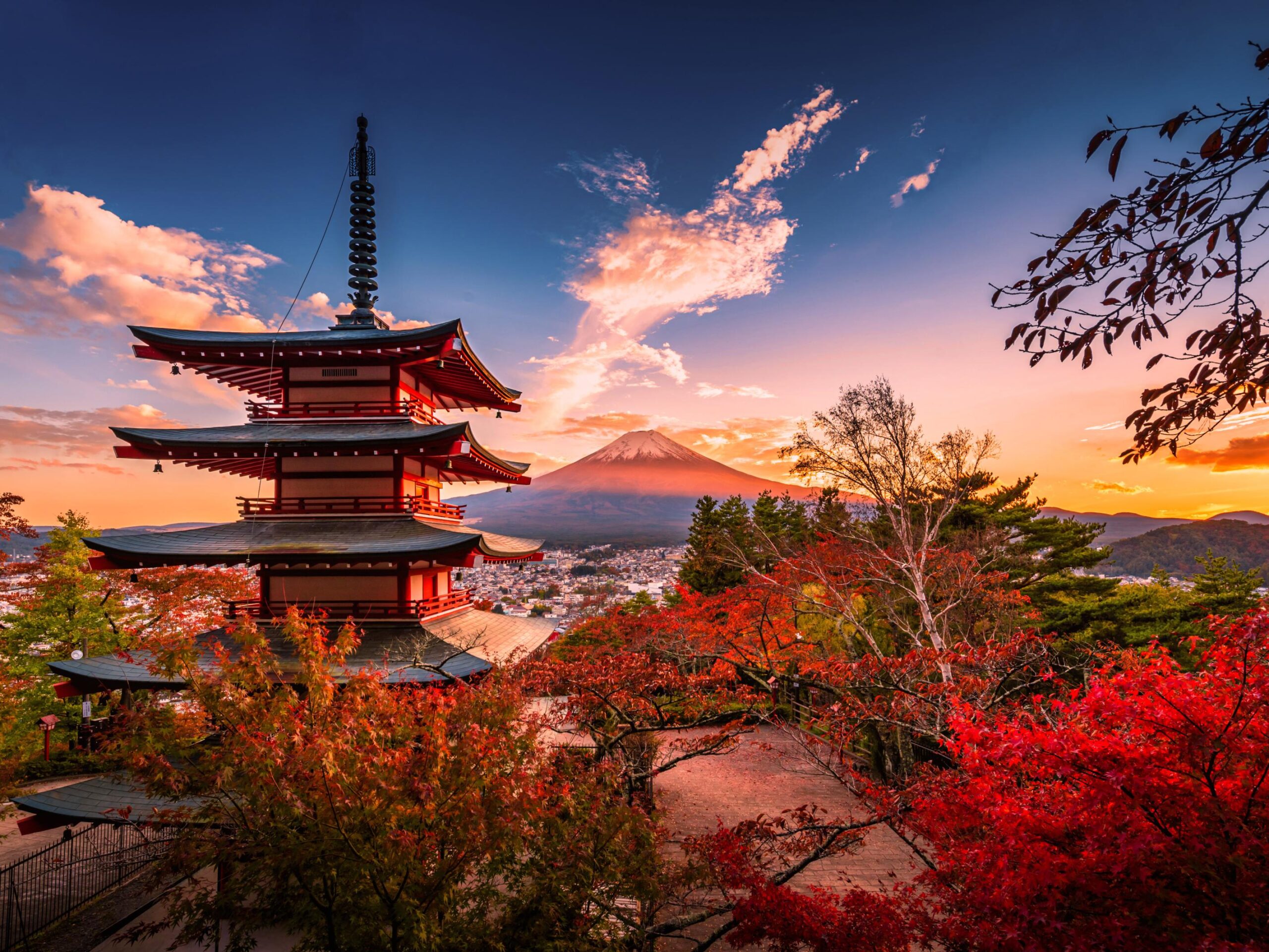 Fünfstöckige Pagode vor herbstlich roten Ahornbäumen, im Hintergrund der schneebedeckte Fuji bei Sonnenuntergang