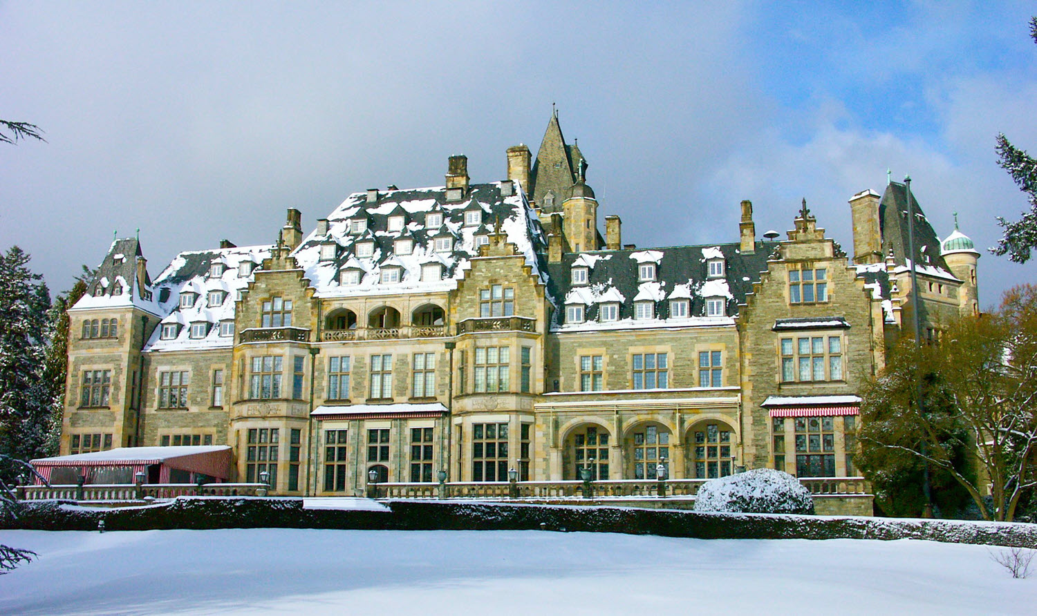 Schloss&auml;hnliches Schlosshotel Kronberg mit verschneitem Dach und Fassade, umgeben von winterlicher Parklandschaft