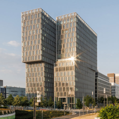 Modernes Bürogebäude des F.A.Z.-Towers mit Glasfassade und Sonnenreflexion, umgeben von Bäumen und Straßen in Frankfurt