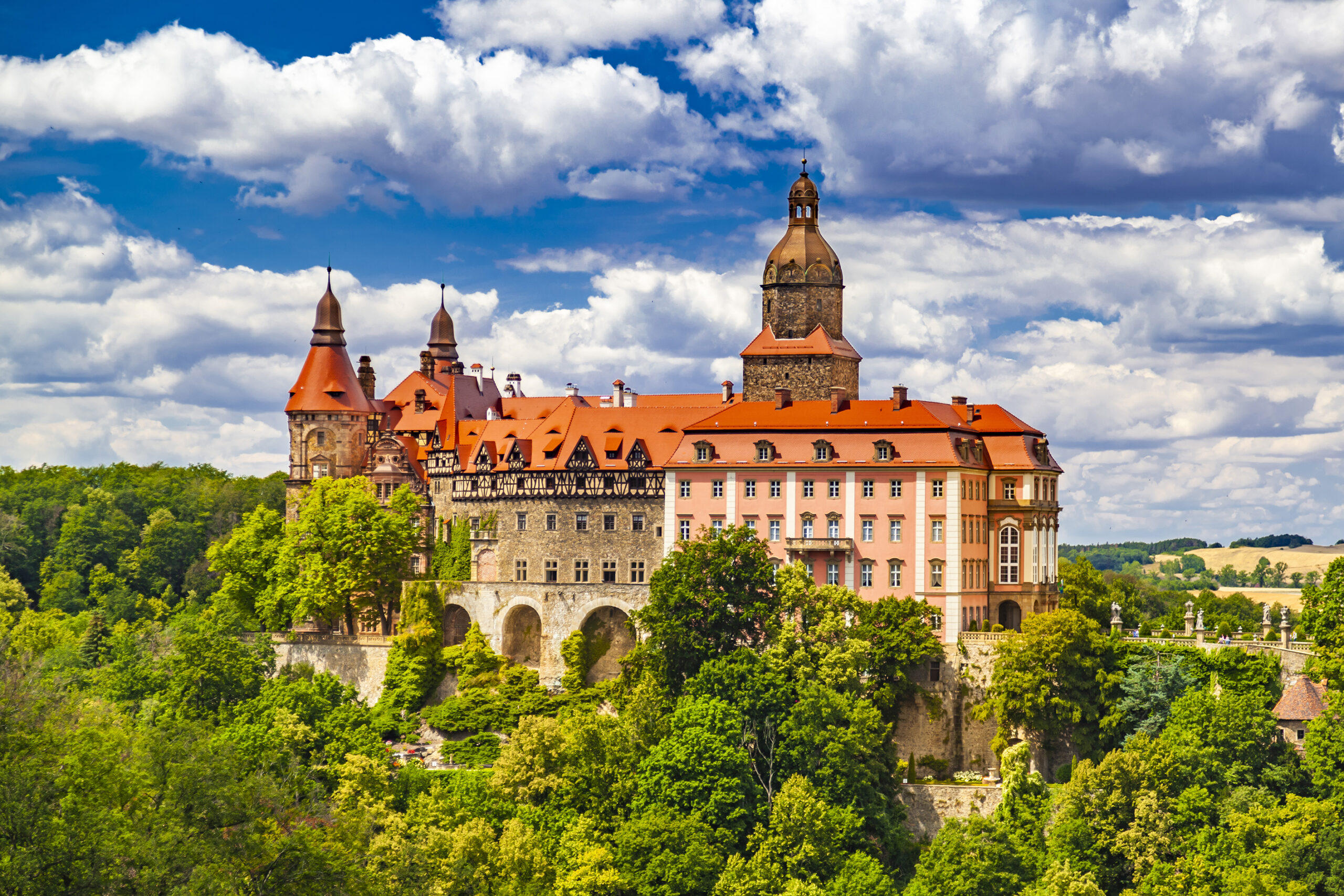 Schloss Fürstenstein mit roten Dächern und Türmen auf bewaldetem Hügel unter blauem Himmel mit weißen Wolken