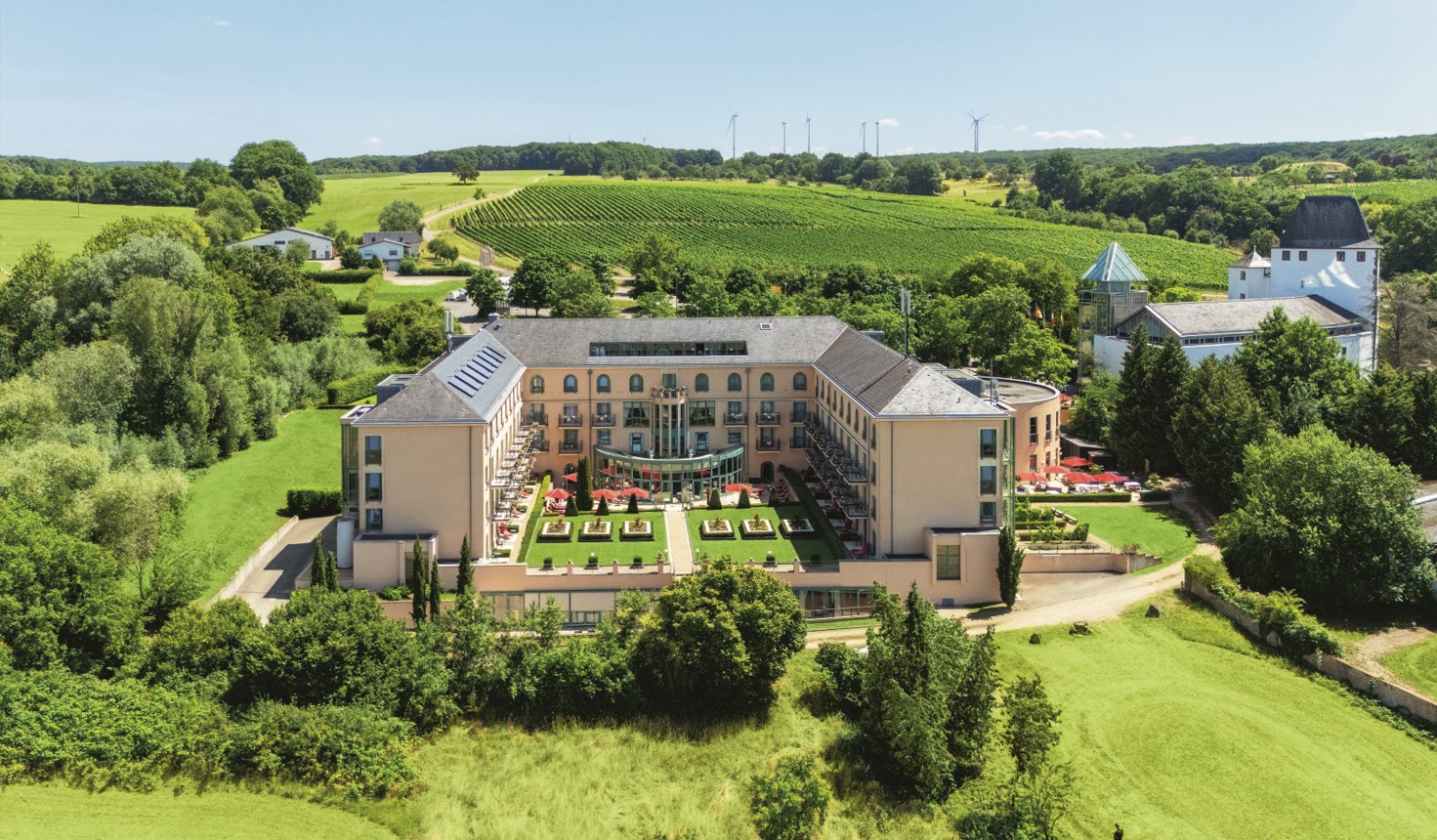 Luxuriöses Schlosshotel mit U-förmigem Gebäude, gepflegtem Garten, umgeben von Weinbergen und grüner Hügellandschaft