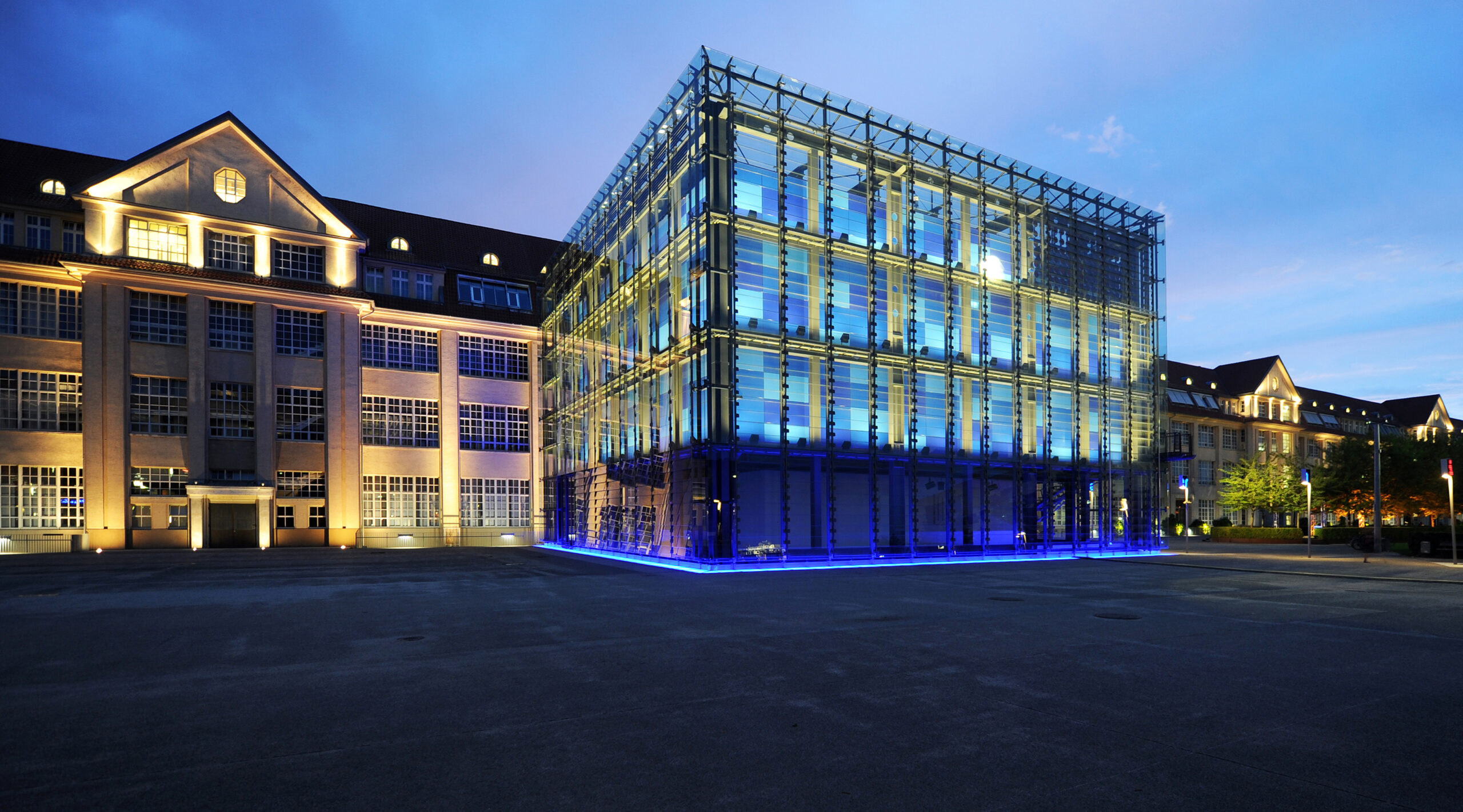 Glasfassade des ZKM Karlsruhe bei Nacht, blau beleuchtet, neben historischer Backsteinarchitektur im Innenhof