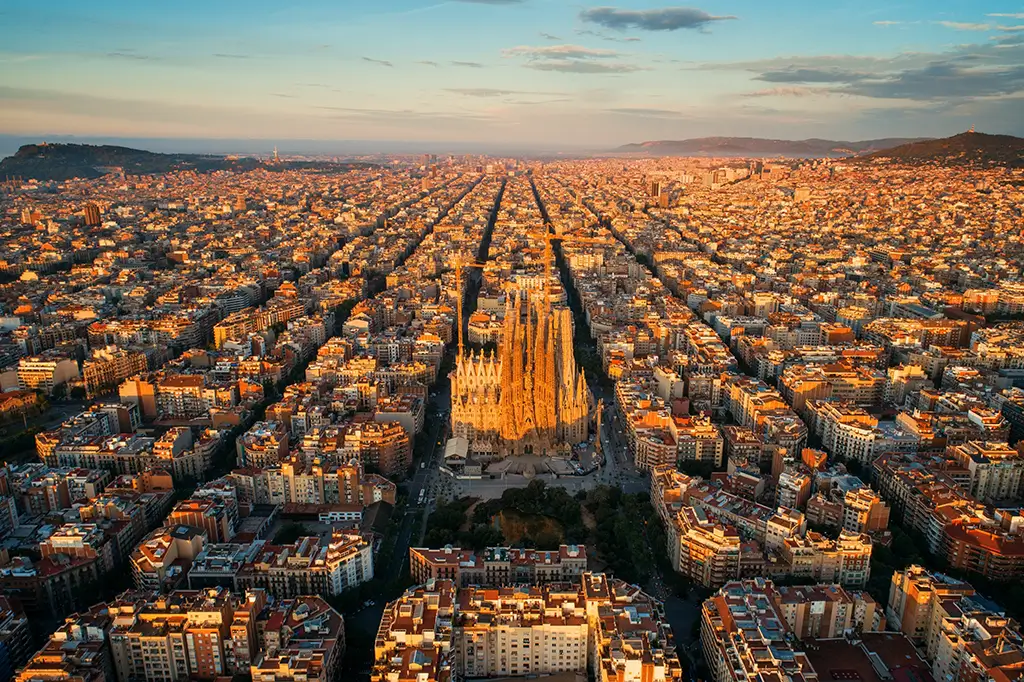 Luftaufnahme der Sagrada Família in Barcelona, Spanien, umgeben von dicht bebauten Stadtvierteln im warmen Licht der untergehenden Sonne.